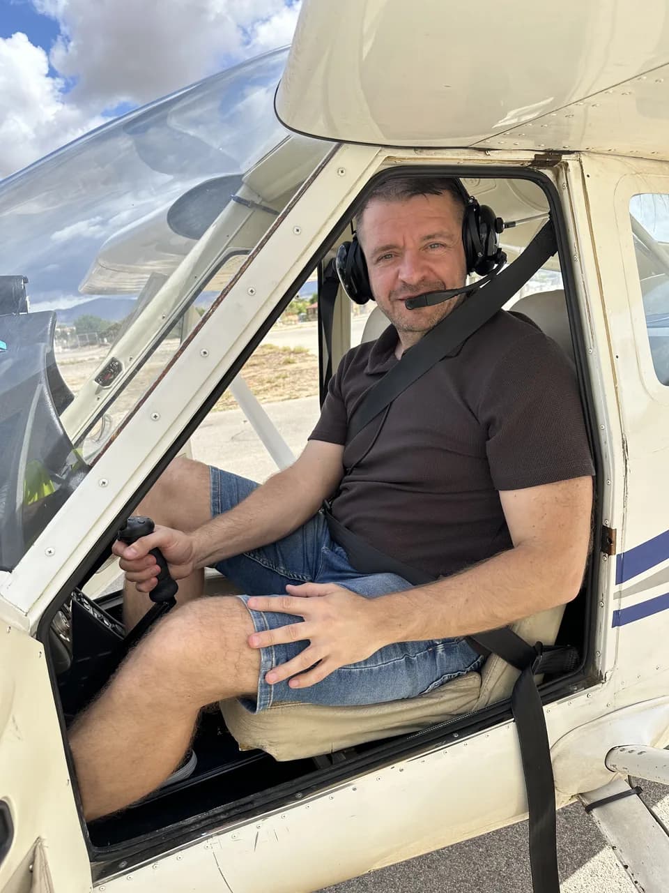 Seated in the cockpit with a headset and a hand on the control stick